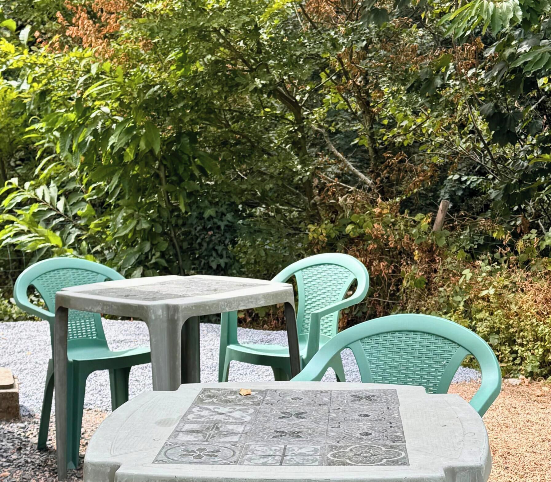 Een tafel en twee stoelen in een openlucht setting, met groen in de achtergrond.