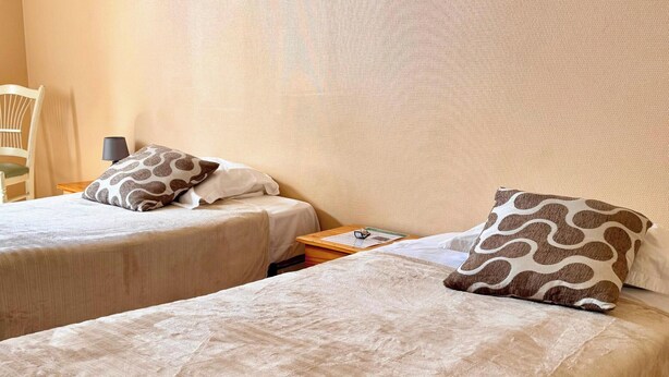 Habitación de hotel con dos camas individuales, cada una con un cojín estampado y una mesita de noche de madera.