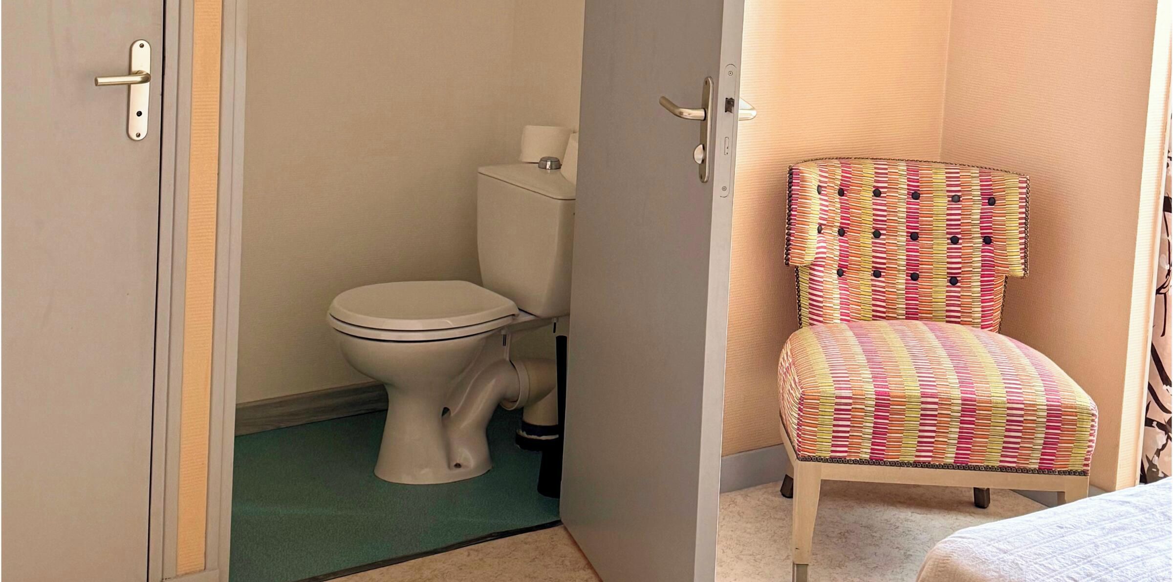 Un baño con inodoro, una silla y una puerta.
