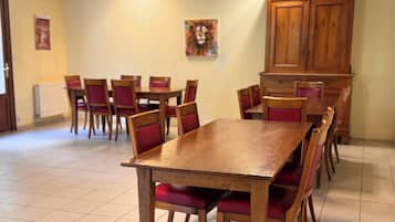 Een eetgedeelte met houten tafels en stoelen, een betegelde vloer en een schilderij aan de muur.