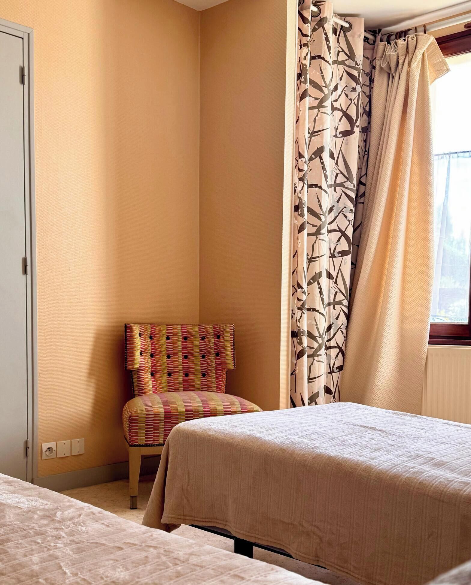 Een hotelkamer met twee bedden, een gestreept fauteuil en een raam met gordijnen.