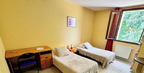 Un alojamiento pequeño, con una habitación individual que incluye un escritorio, dos camas individuales, una silla y una ventana con cortinas.