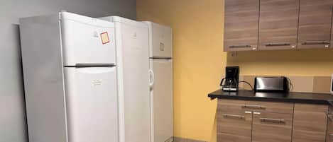 Una cocina con dos refrigeradores blancos, armarios de madera, una cafetera y un tostador.