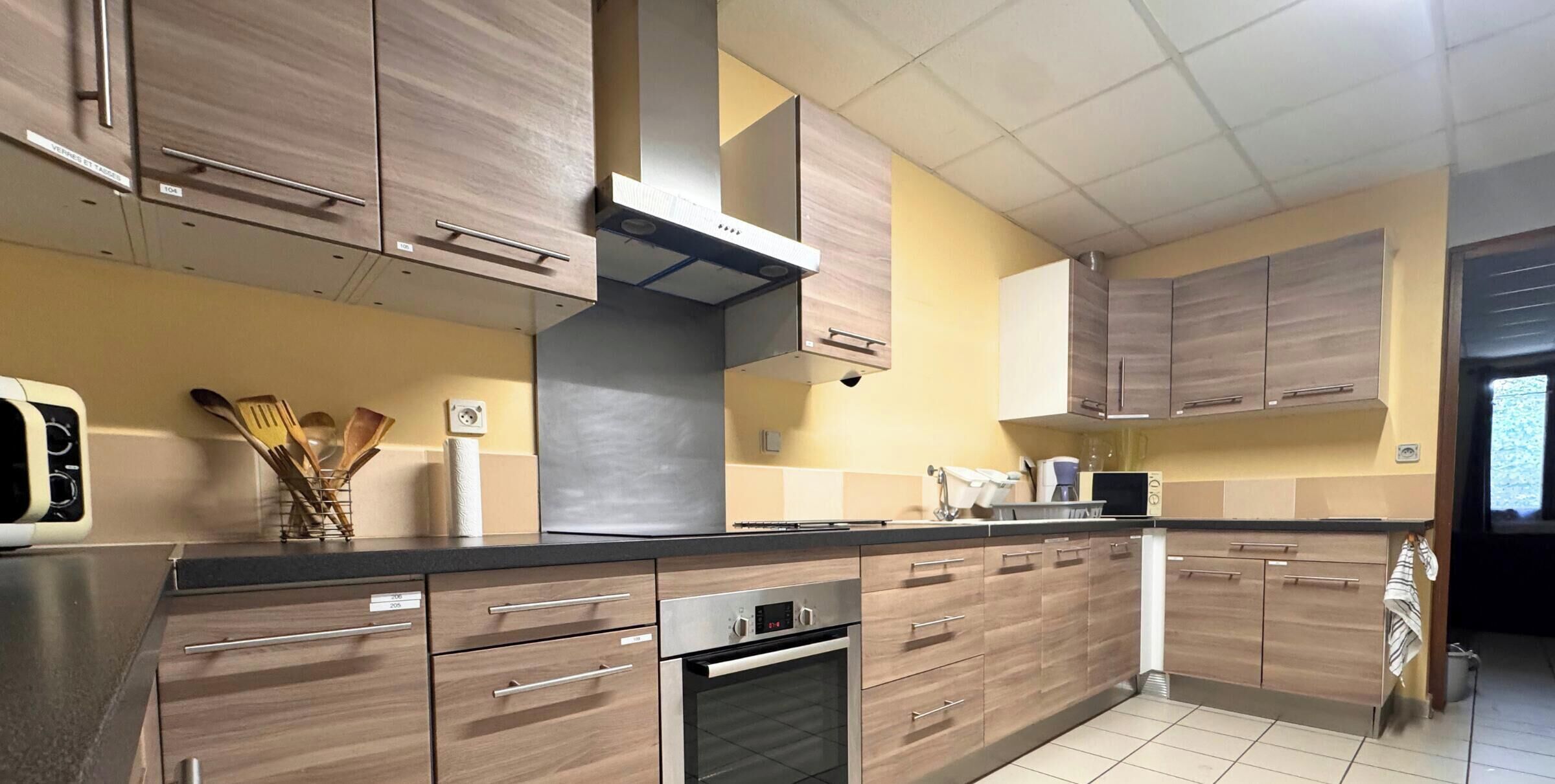 Une cuisine avec des armoires en bois, une hotte de cuisinière en acier inoxydable et un dosseret carrelé.