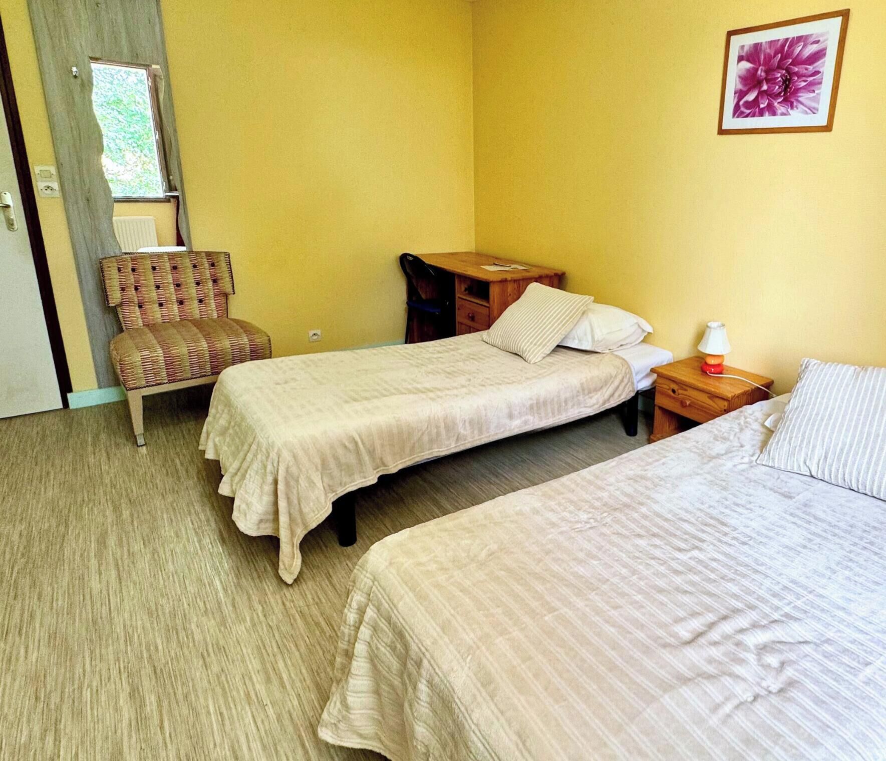 Une chambre avec deux lits, une chaise, un bureau et une fenêtre.