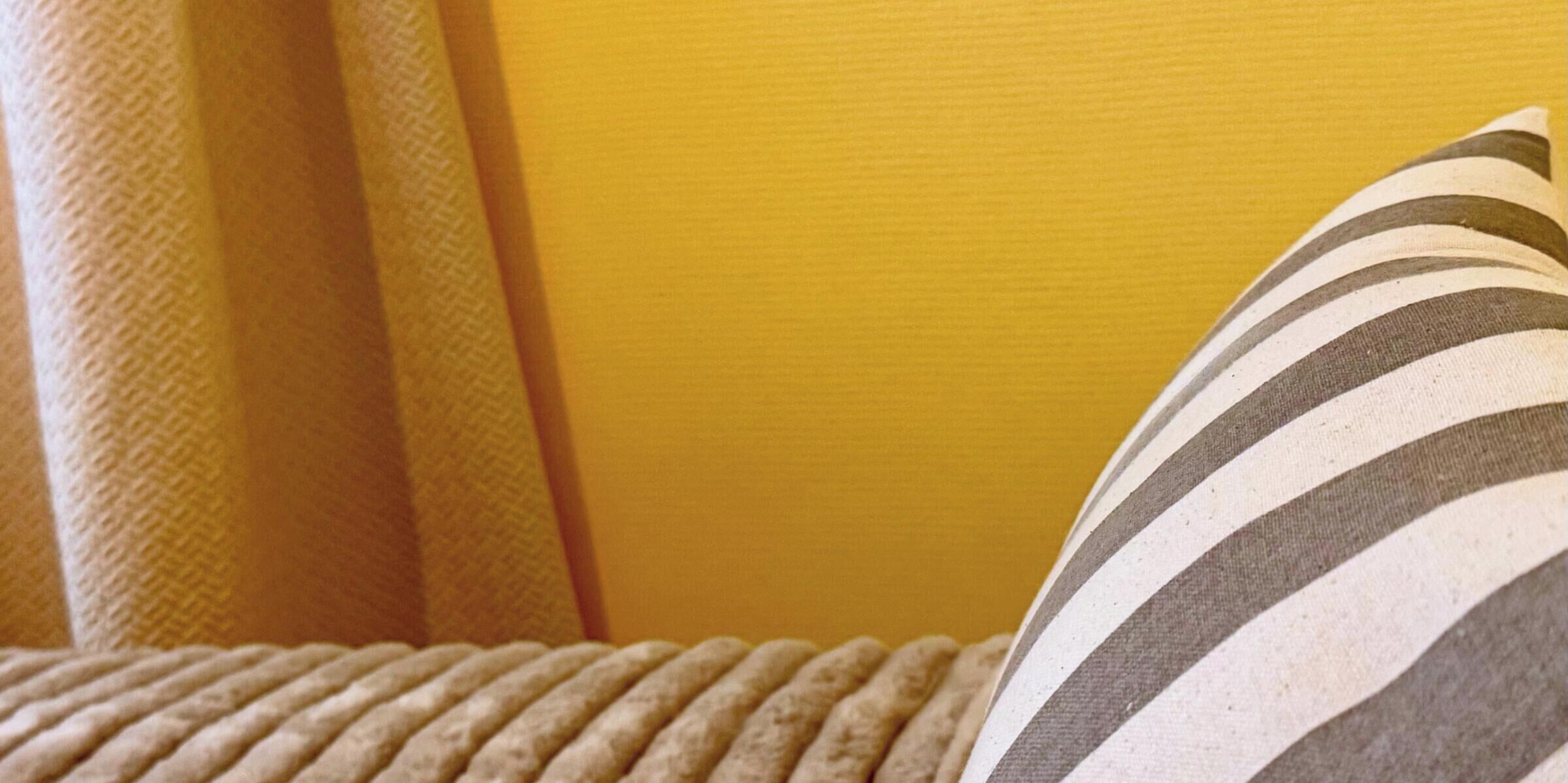 Detailaufnahme eines gestreiften Kissens auf einer strukturierten Couch vor einer gelben Wand.