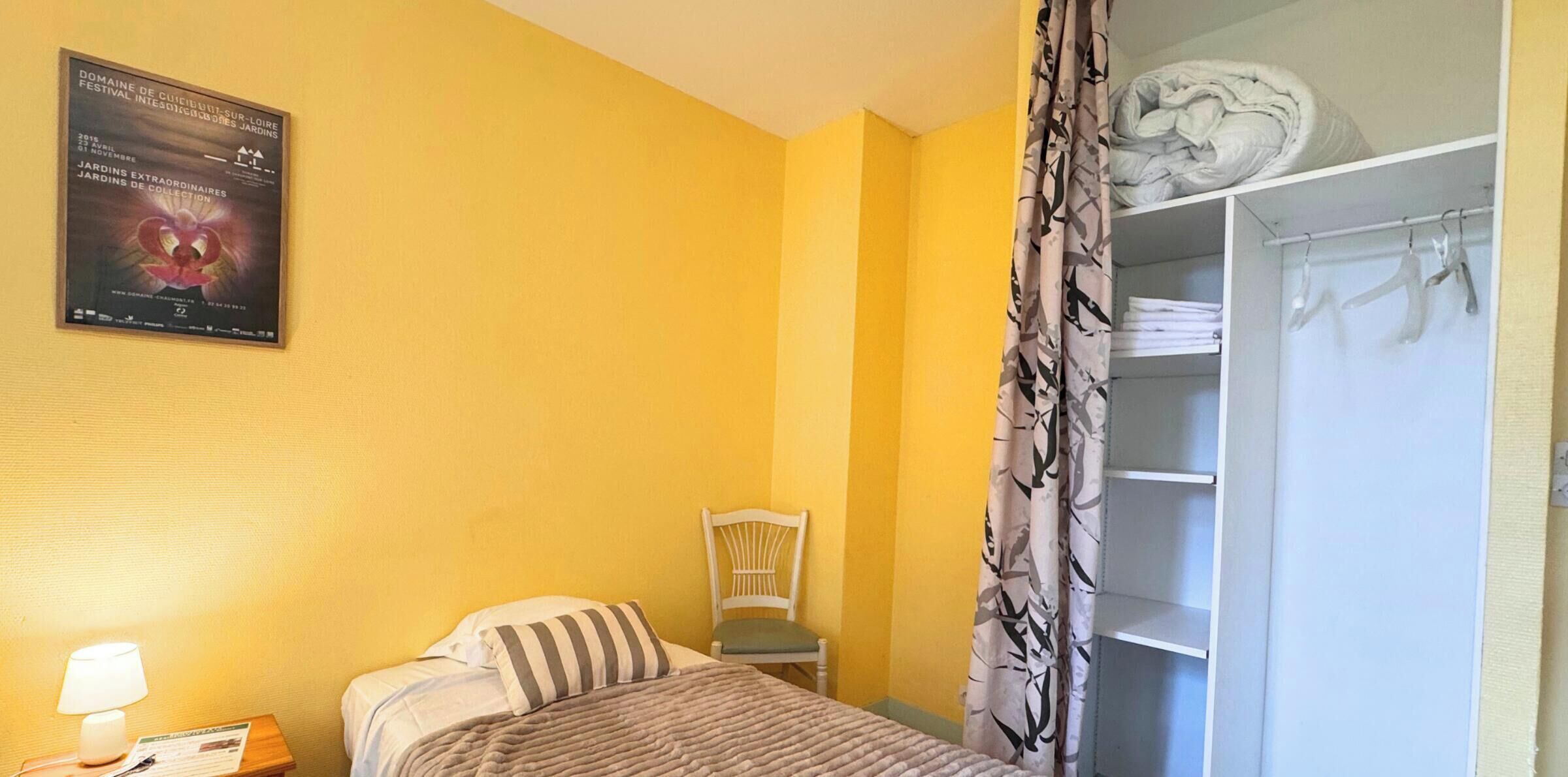 Une chambre d’hôtel avec un lit, une chaise, une armoire et une affiche au mur.