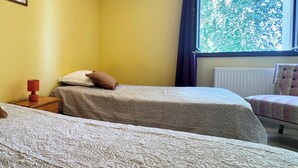 Quarto com duas camas, janela com vista para árvores e uma cadeira.