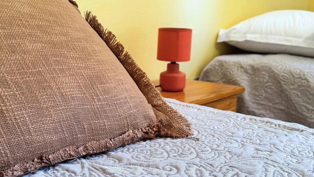 Cama com travesseiro marrom texturizado e colcha branca estampada.
