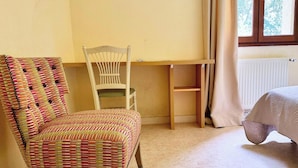 A room with a wooden desk, a chair with a striped cushion, a bed with a quilt, and a window with curtains. - Room 109 - Le Bas Mont Residence (Moulay)
