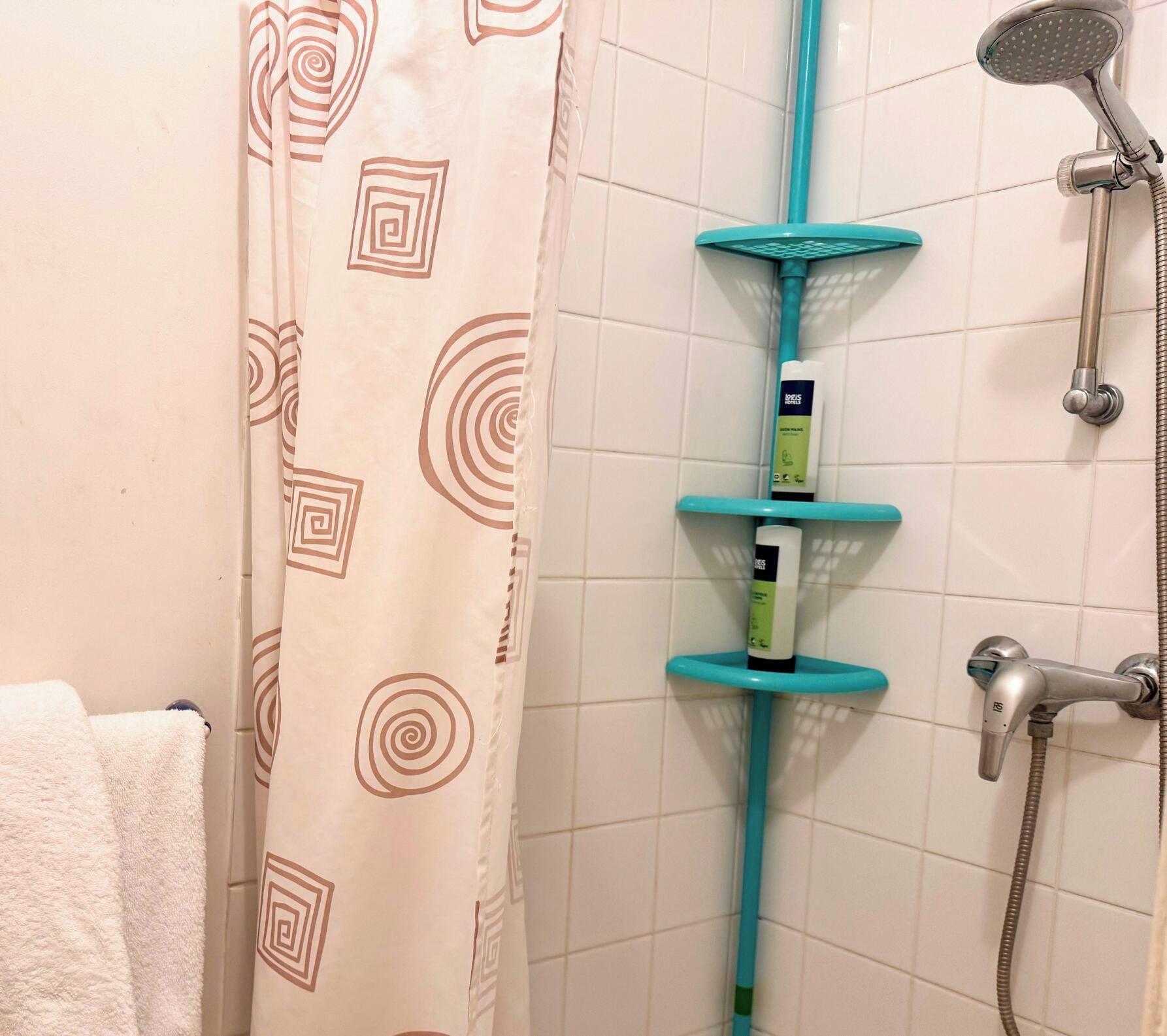 Une salle de bain avec une douche, un porte-serviettes et une étagère contenant des articles de toilette.