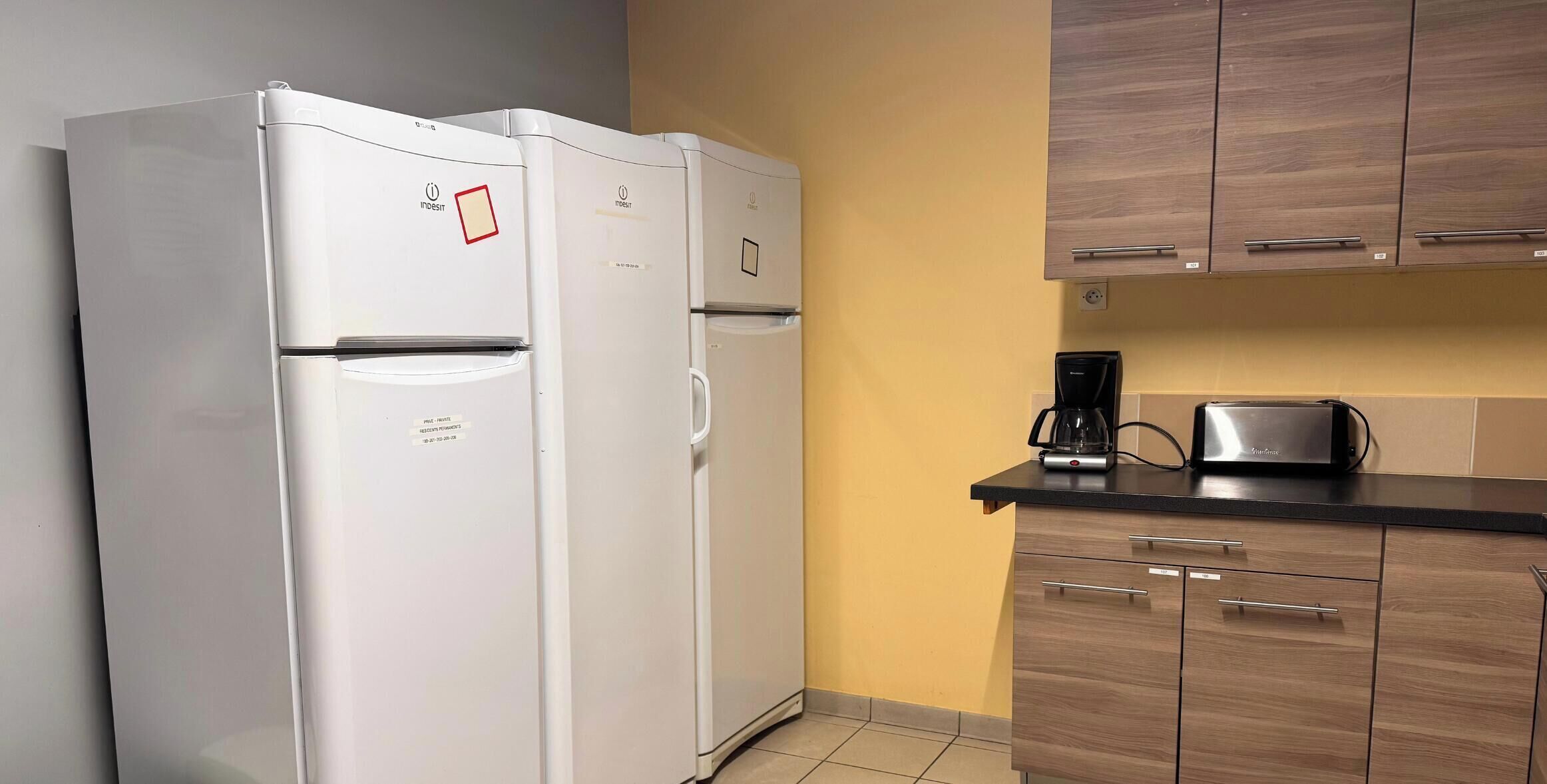 A kitchen with two white refrigerators, wooden cabinets, a coffee maker, and a toaster.