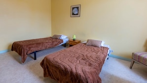 Una habitació amb dos llits individuals, una petita taula de nit amb una làmpada i un quadre encimbellat a la paret.