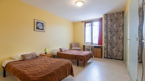 Un dormitori amb dos llits, un escriptori, una cadira, una finestra amb cortines i una porta amb cortina estampada.