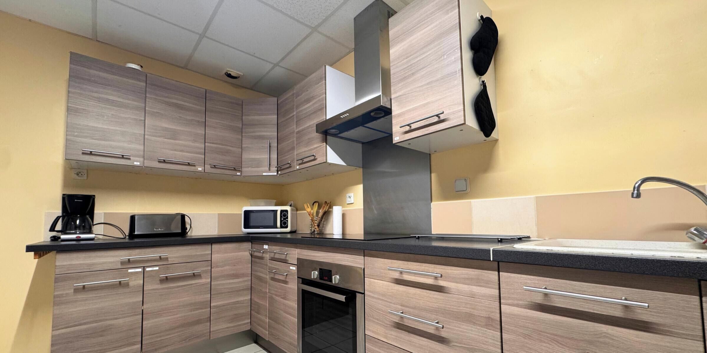 A modern kitchen with wooden cabinets, a microwave, a coffee maker, and a sink.