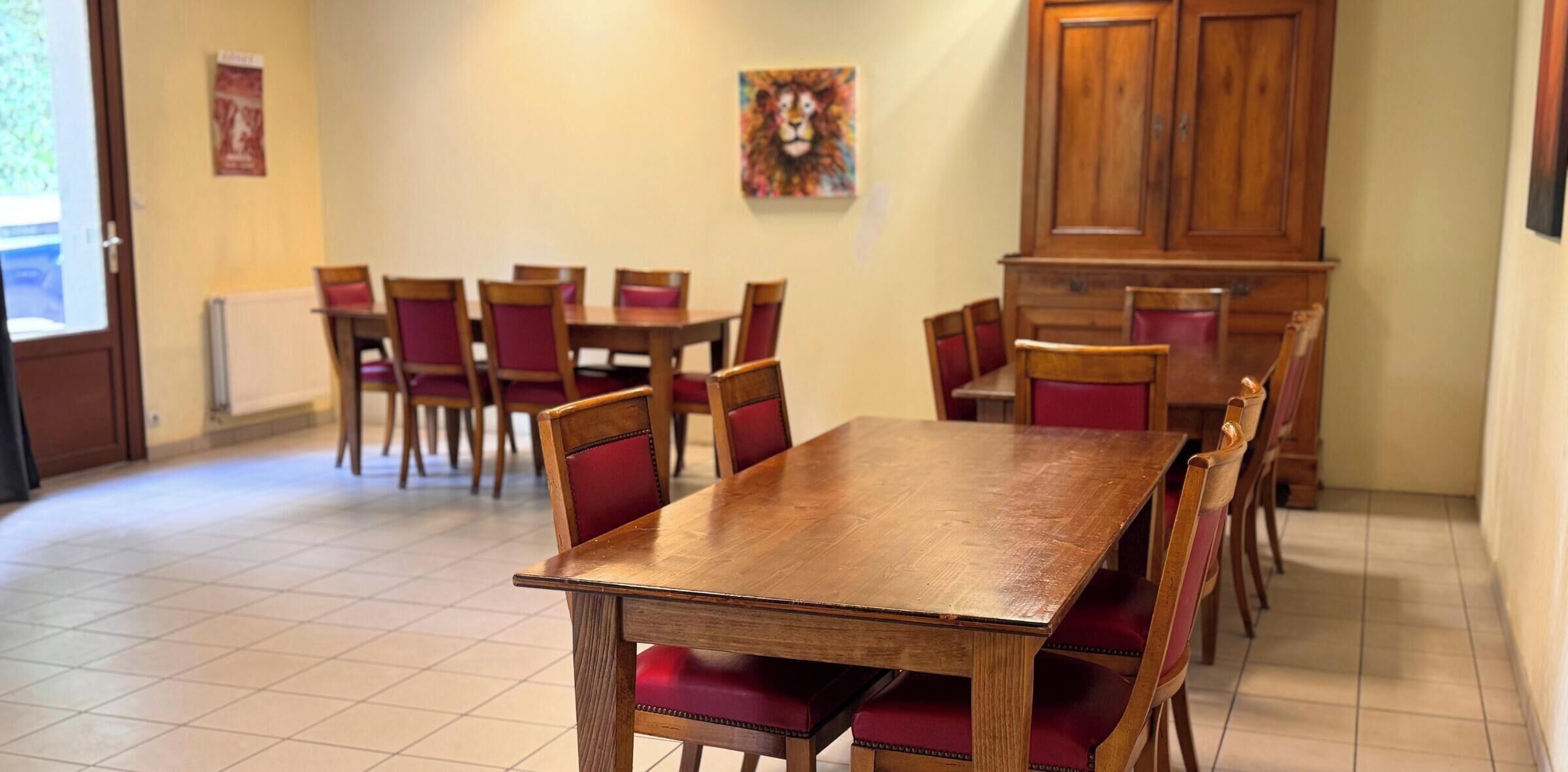 A dining area with wooden tables and chairs, a tiled floor, and a painting on the wall.