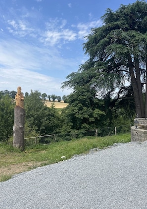 Una estàtua sobre un pedestal, un camí de grava i un arbre gran.