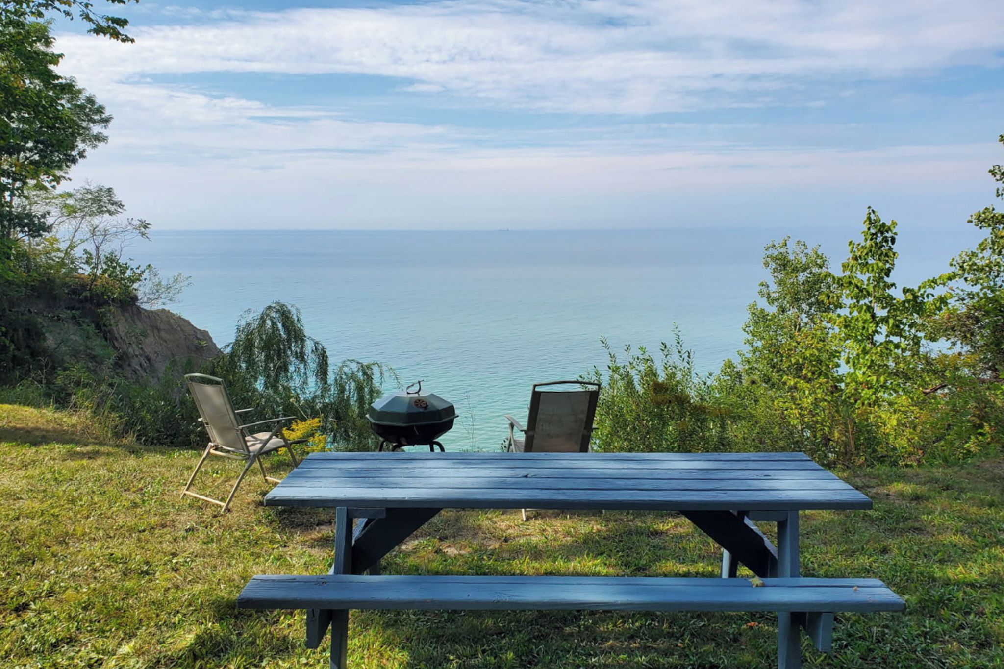 Une table de pique-nique avec deux chaises et un barbecue, donnant sur une étendue d’eau.