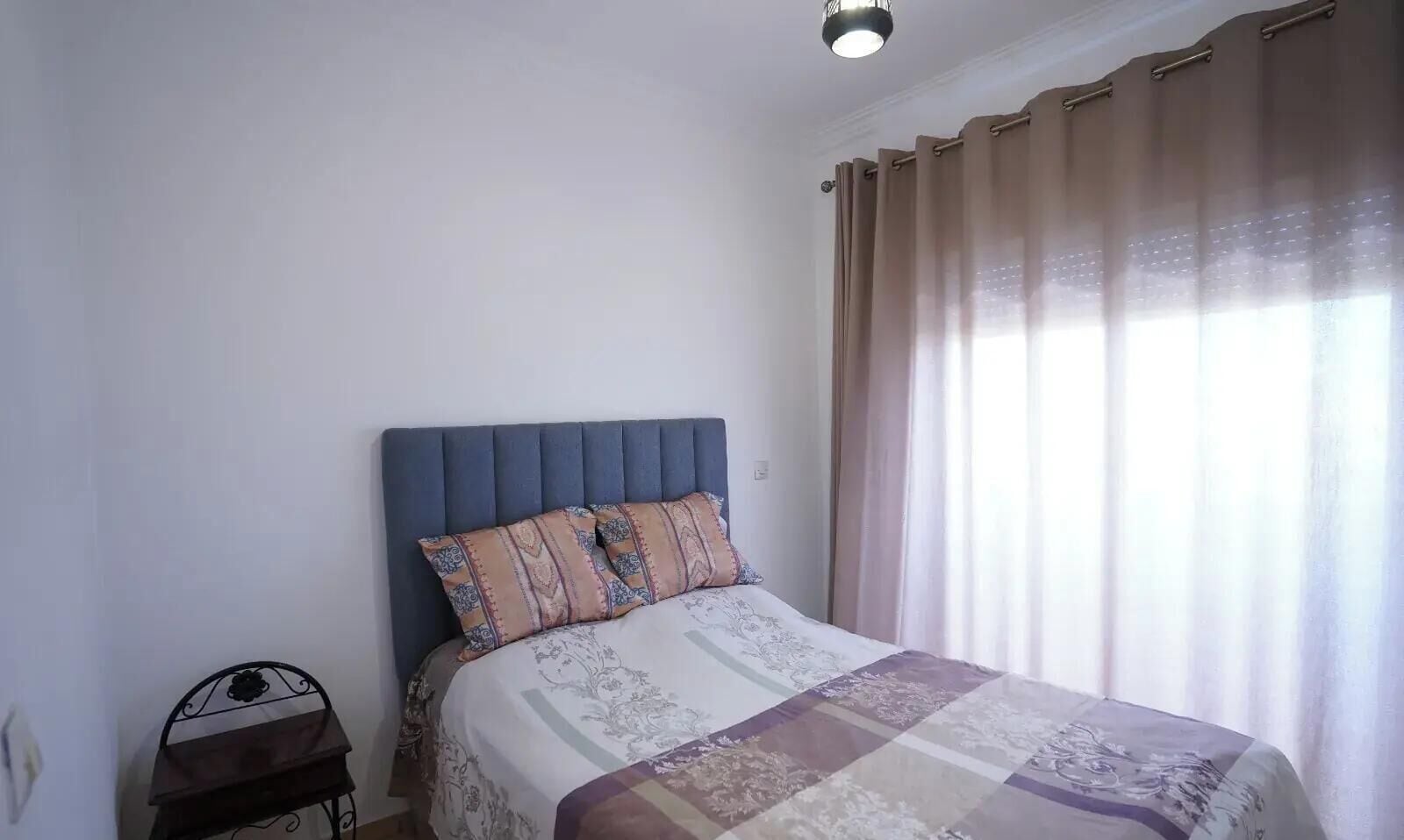 Ein Schlafzimmer mit einem Bett, einem Nachttisch und einem Fenster mit Vorhängen.