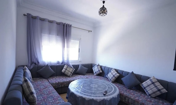 A modern living room with a sectional sofa, patterned rug, and a round coffee table. - Charming 2-Bedroom Apartment in Martil,Morocco (Martil)