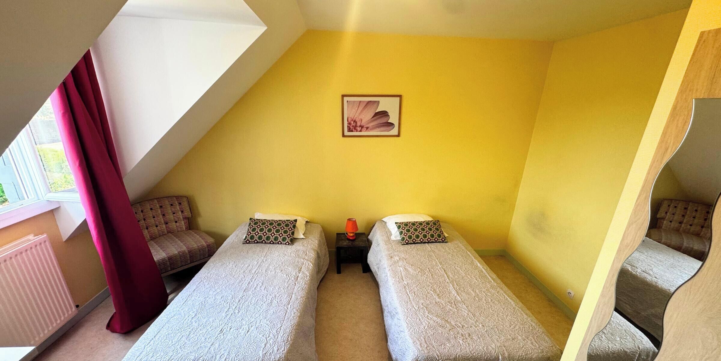 Une petite pièce triangulaire, avec deux lits simples, une petite table et un tableau accroché au mur.