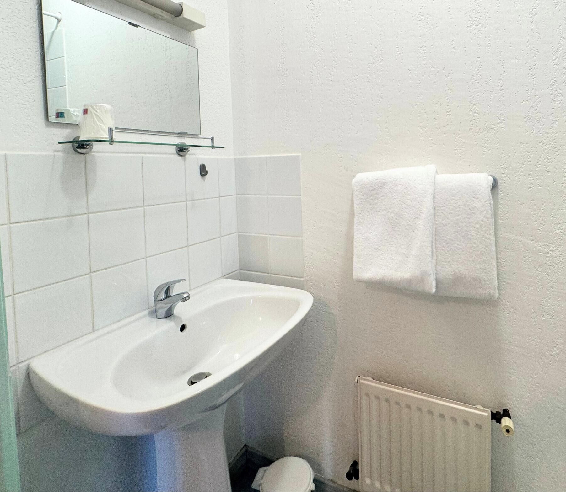 Un baño con un lavamanos blanco, un espejo, un toallero con dos toallas y un radiador.