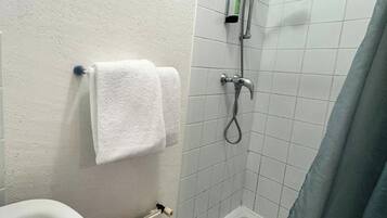 Une petite salle de bain avec une baignoire blanche, une douche équipée d’un pommeau de douche amovible et des toilettes.