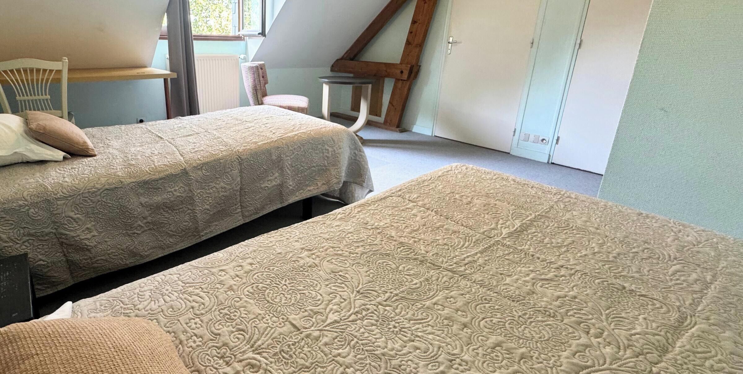 Ein Zimmer mit zwei Betten, einem Sessel, einem kleinen Tisch und einem Fenster.