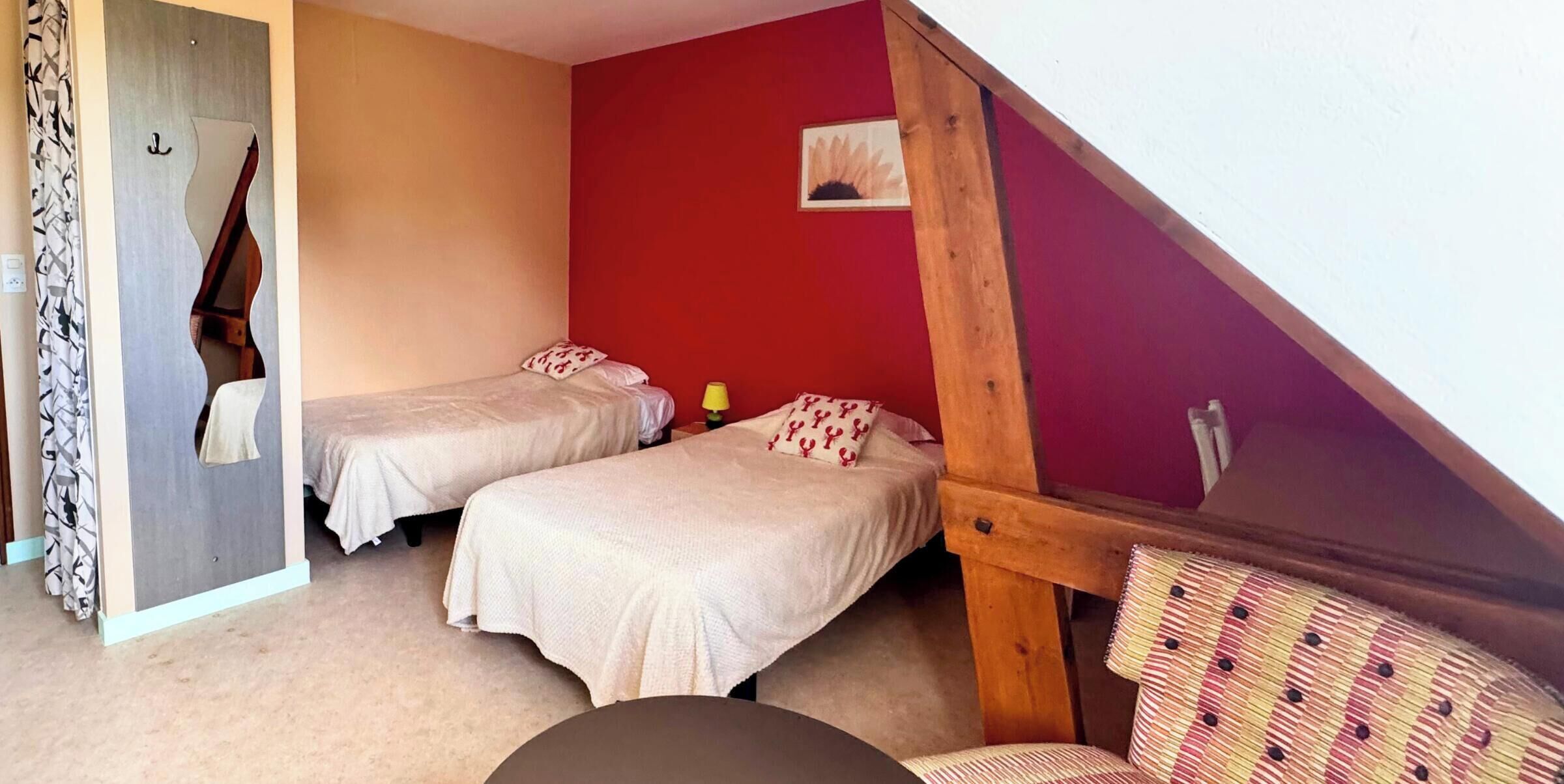 A bedroom with two beds, a wooden staircase, and a red wall.
