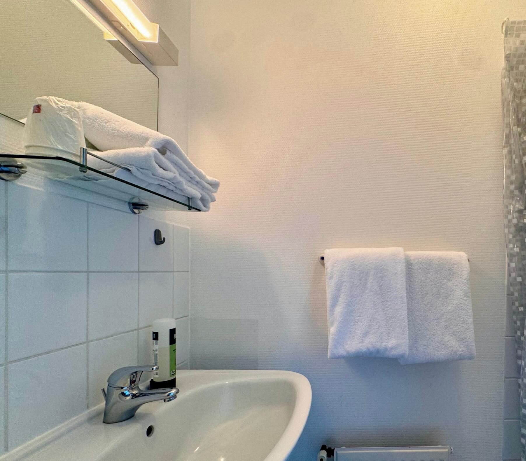 A bathroom with a white sink, a mirror, and a towel rack with folded towels.