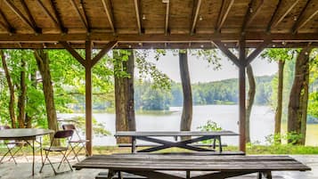 A covered picnic area with a view of a lake surrounded by trees.