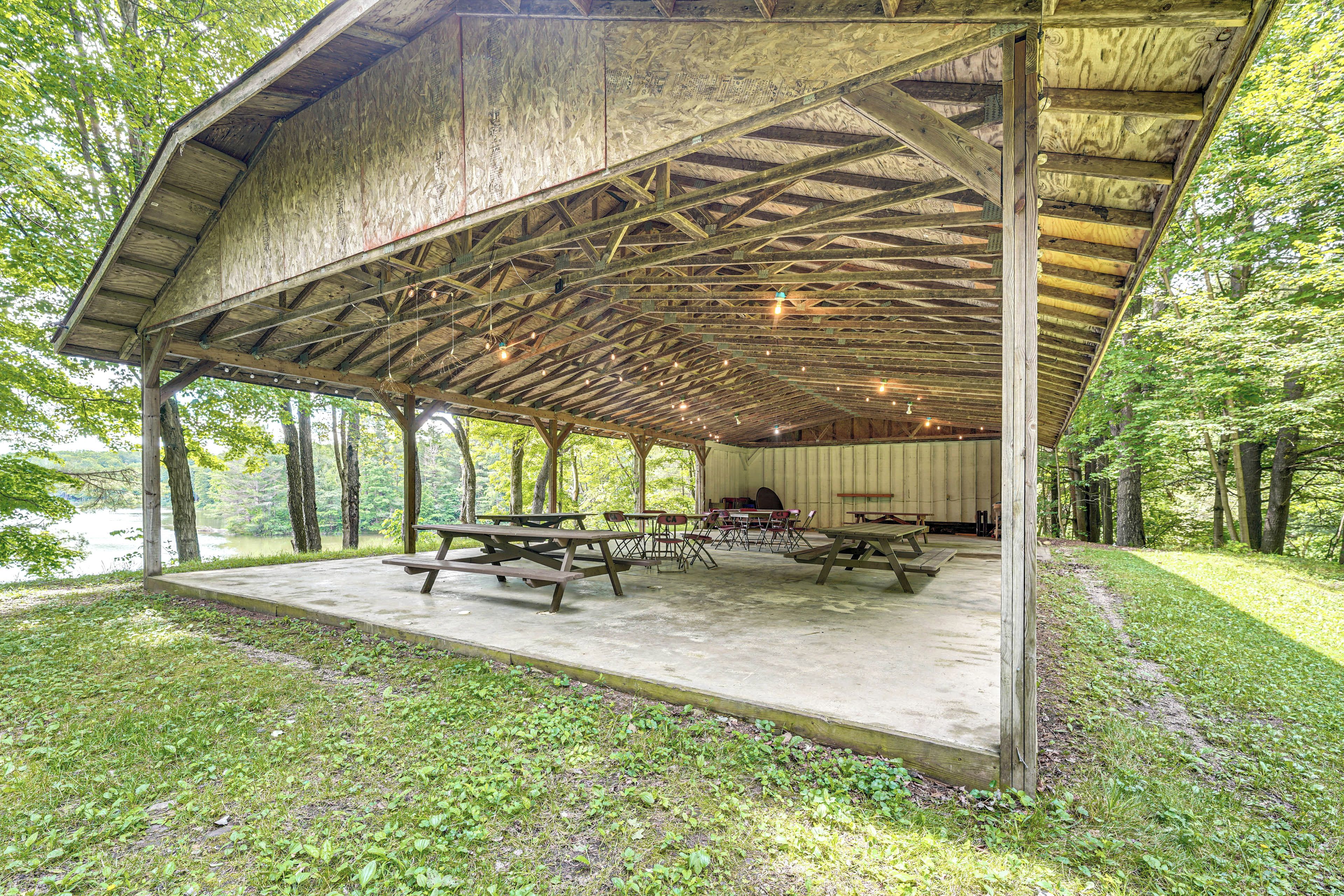 A covered picnic area with picnic tables and chairs, surrounded by trees and a body of water.