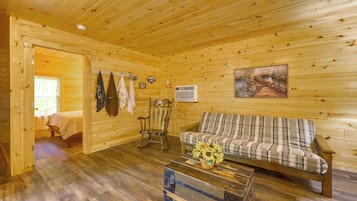 A wooden cabin interior with a bed, a rocking chair, a sofa, and a rustic wooden chest.
