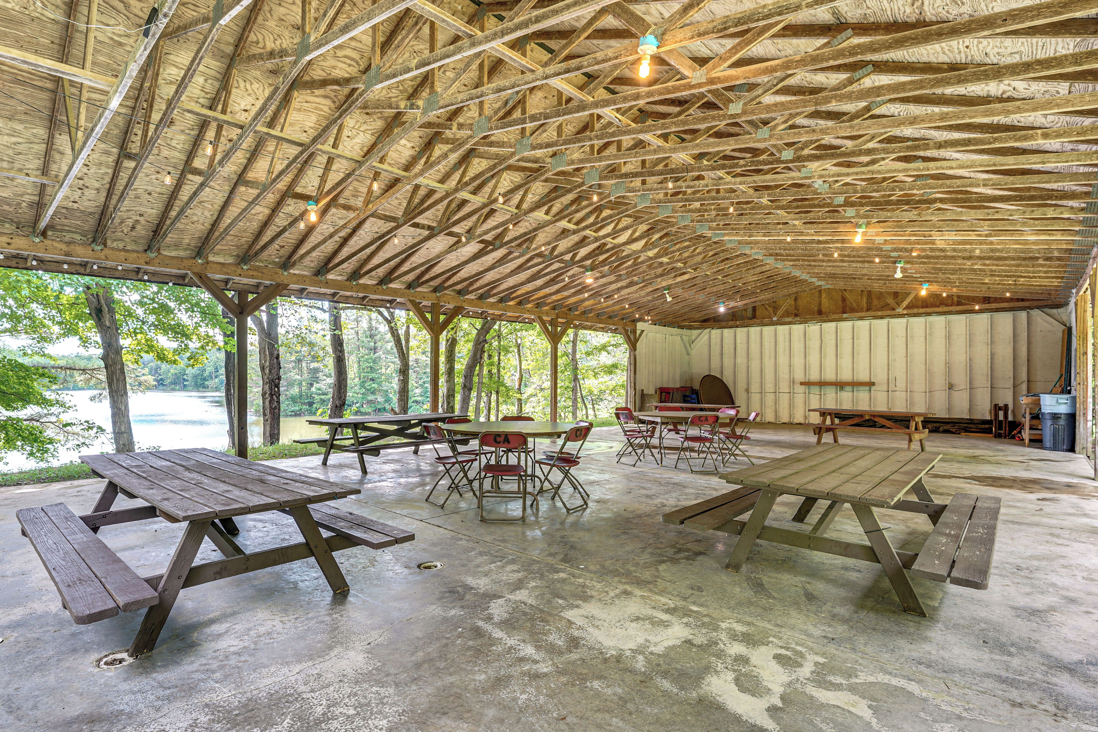 Un pavillon extérieur doté de tables et de chaises pour pique-nique, d’une scène et offrant une vue sur un lac.