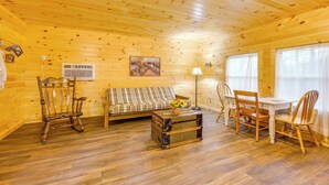 Un interior de madera con un sofá, sillas, una mesa de comedor, una lámpara y un cuadro en la pared.