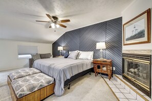 A bedroom with a bed, a nightstand, a lamp, a bench, a fireplace, and a ceiling fan. - Game Room, Deck + Yard! Cadillac Family Escape (Cadillac)