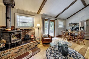 A cozy living room with a fireplace, a dining area, and a kitchen with modern appliances. - Cadillac Escape w/ Game Room, Deck & Yard! (Cadillac)
