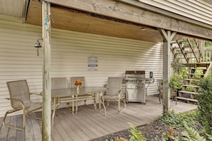 A covered outdoor patio with a table and chairs, a grill, and a signboard. - Game Room, Deck + Yard! Cadillac Family Escape (Cadillac)