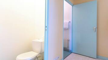 Une petite salle de bain étroite, avec des toilettes, un radiateur et une porte donnant sur une autre pièce.