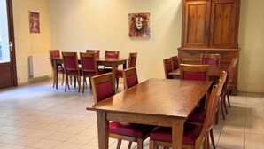 A dining area with wooden tables and chairs, a tiled floor, and a painting on the wall. - Room 105 - Le Bas Mont Residence (Moulay)