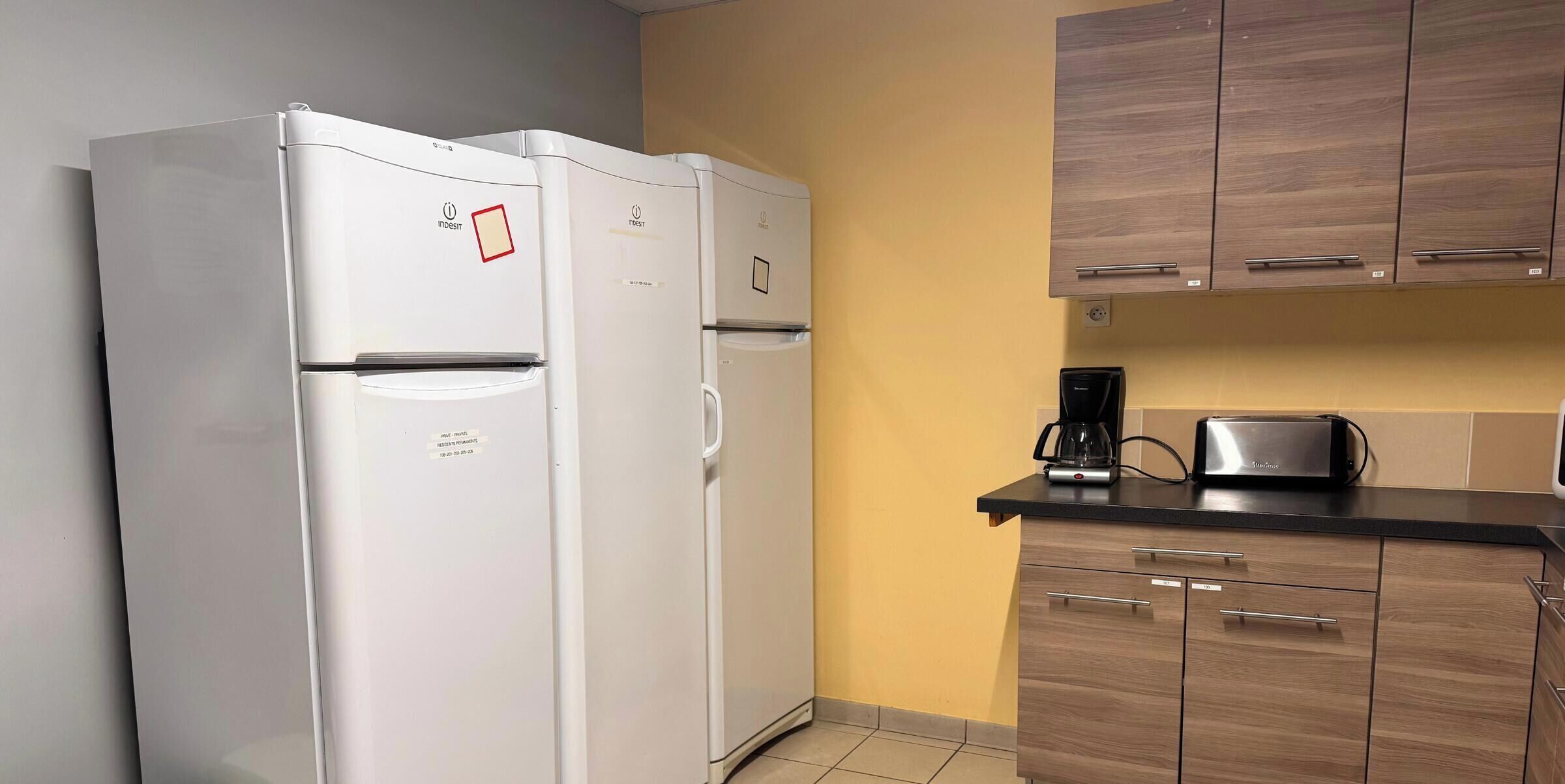 A kitchen with two white refrigerators, wooden cabinets, a coffee maker, and a toaster.