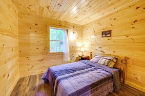 Une chambre dans un chalet en bois, avec un lit, une table de chevet, une lampe, une fenêtre et une pancarte de bienvenue.