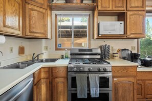 A kitchen with wooden cabinets, a stainless steel stove, a microwave, and a window overlooking a covered outdoor area. - All Seasons Lodge: Family Haven in Big Bear (Big Bear Lake)