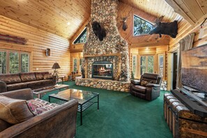 A log cabin interior with a stone fireplace, leather furniture, and a television. - All Seasons Lodge: Family Haven in Big Bear (Big Bear Lake)