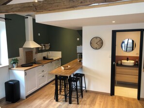 A modern kitchen with white cabinets, a wooden countertop, a black trash bin, and a round wall clock. - Delacouraugrenier 1 Vacation Rentals (Chauvigny)