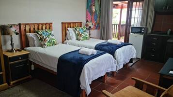 A hotel room with two beds, a desk, a chair, a TV, and a painting on the wall.