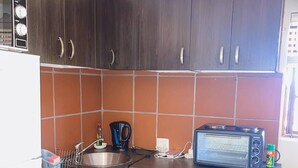 Une cuisine compacte avec des meubles de rangement en bois foncé, un évier en acier inoxydable, un four à micro-ondes et une bouilloire.