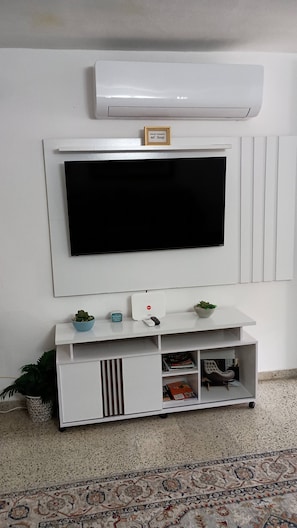 Eine weiße Unterhaltungseinrichtung mit einem flachbildfernseher darüber, einer kleinen Pflanze und einem gerahmten Zitat an der Wand.