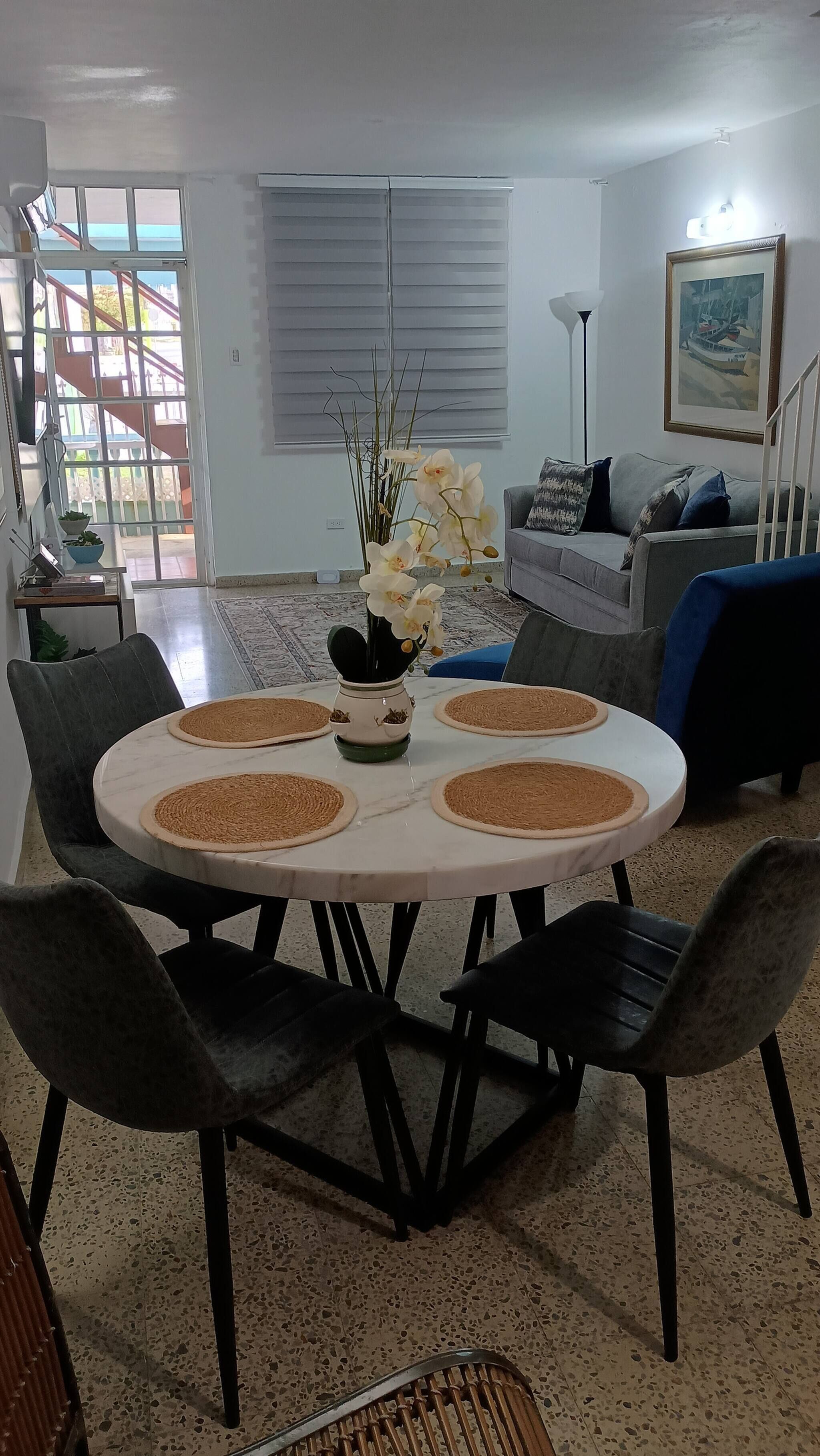 Un coin repas avec une table ronde, des chaises et un vase rempli de fleurs.