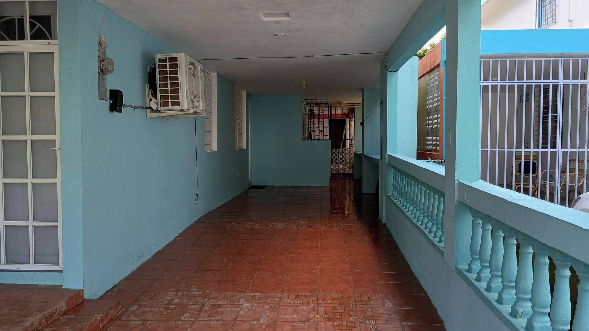 Um corredor com piso de azulejos, uma porta branca e uma janela com grade de metal.